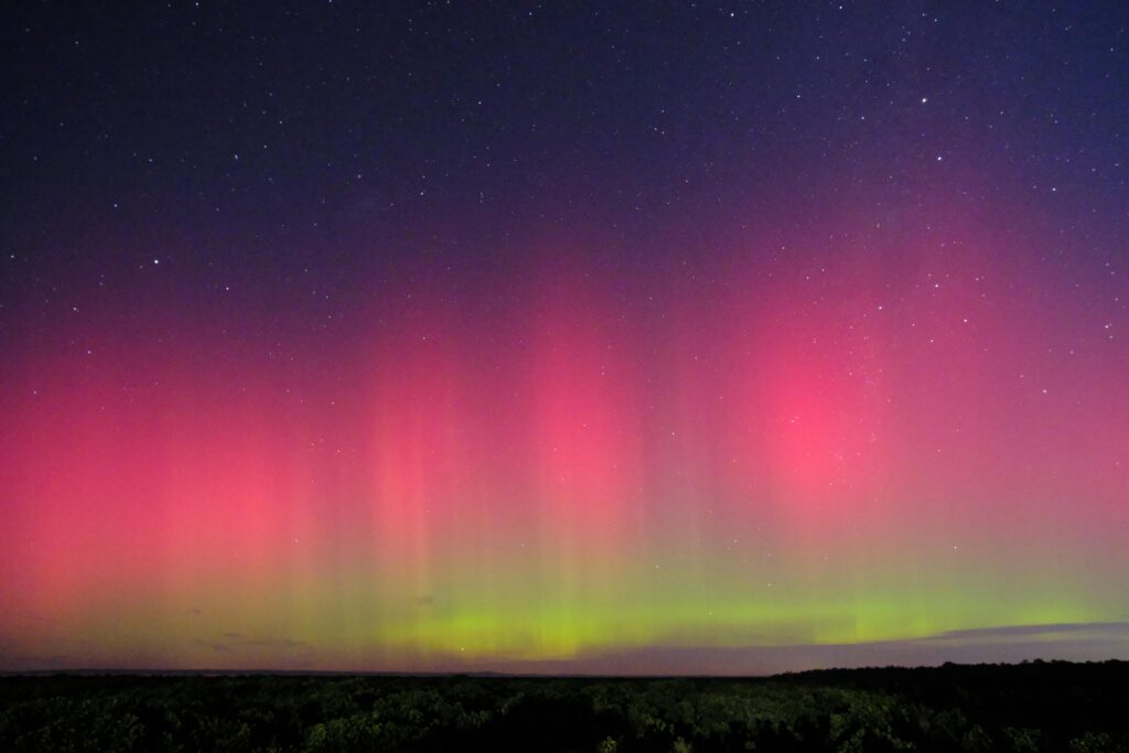 A vivid display of the aurora australis (Southern Lights) glowing in green and purple waves across a clear night sky, gently illuminating a quiet, open field below.
